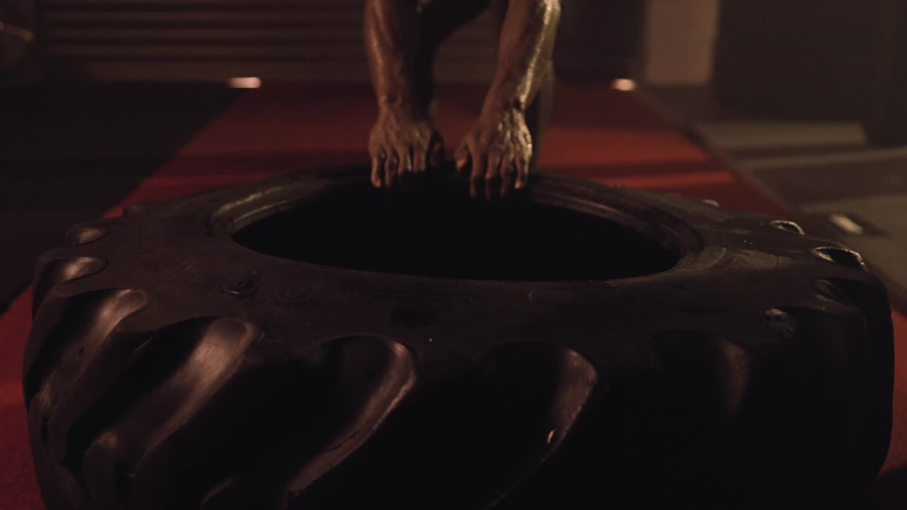 一个精英非裔美国健美运动员的高端镜头，表演一个重量级轮胎/轮胎拉锻炼。设置在一个穆迪，低关键照明混合武术健身房散射的阴霾视频素材