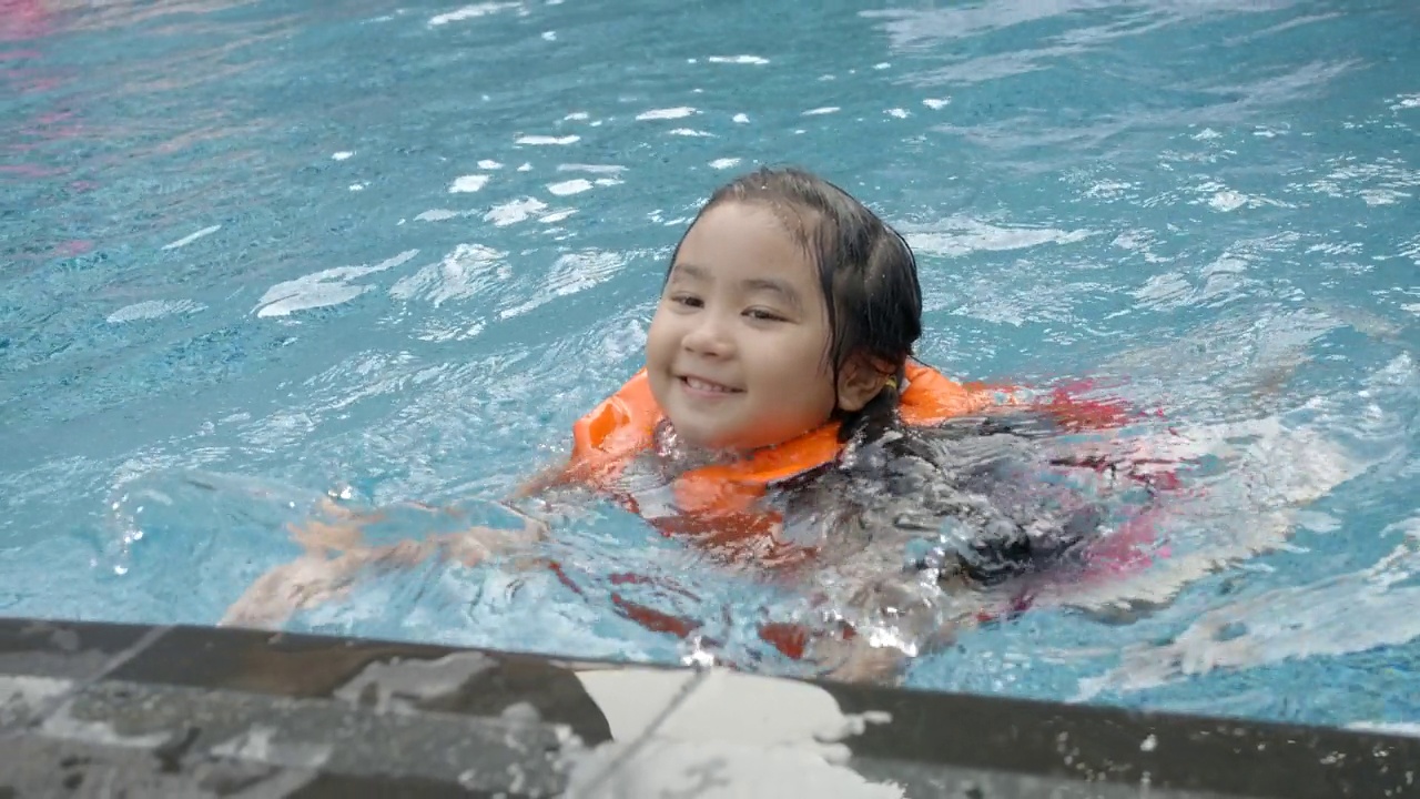 快乐的亚洲小女孩穿着泳装和救生衣学习游泳和在游泳池里玩水，微笑快乐和乐趣。暑假休闲活动或儿童假期旅游视频下载