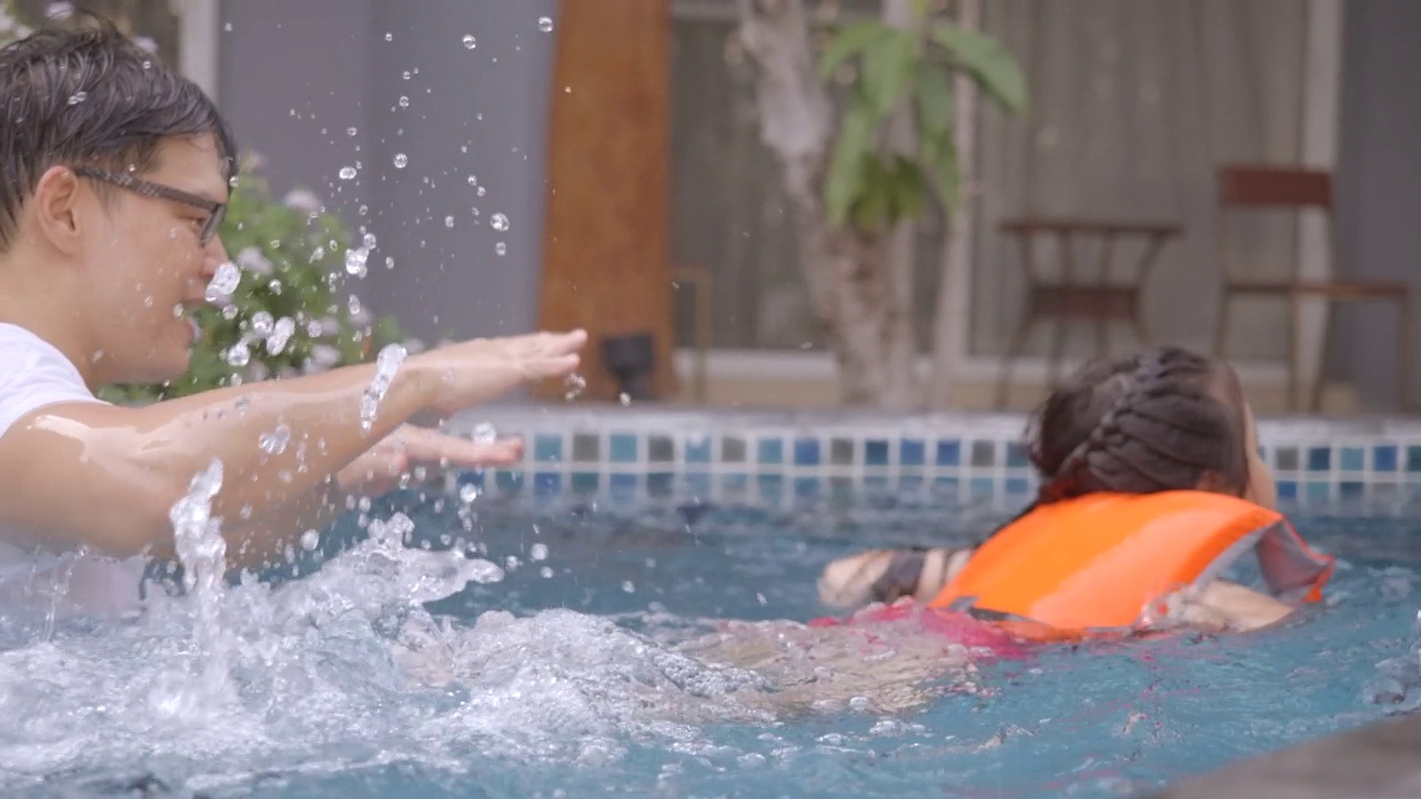 孩子们在暑假里喜欢做各种活动。亚洲家庭，父亲正在游泳池教游泳，带着女儿玩水。教练教学生游泳，假期快乐，乐趣无穷。视频素材