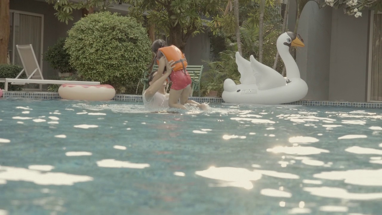 亚洲家庭，爸爸和女儿穿着泳装和救生衣，在游泳池里一起玩水，快乐而有趣的假期。父亲抱起女儿，转过身来。家庭度假活动视频素材