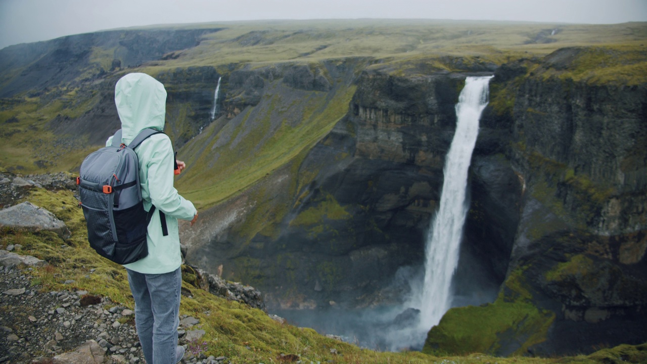 在冰岛高地上，一名女子背着背包欣赏海弗斯瀑布视频素材