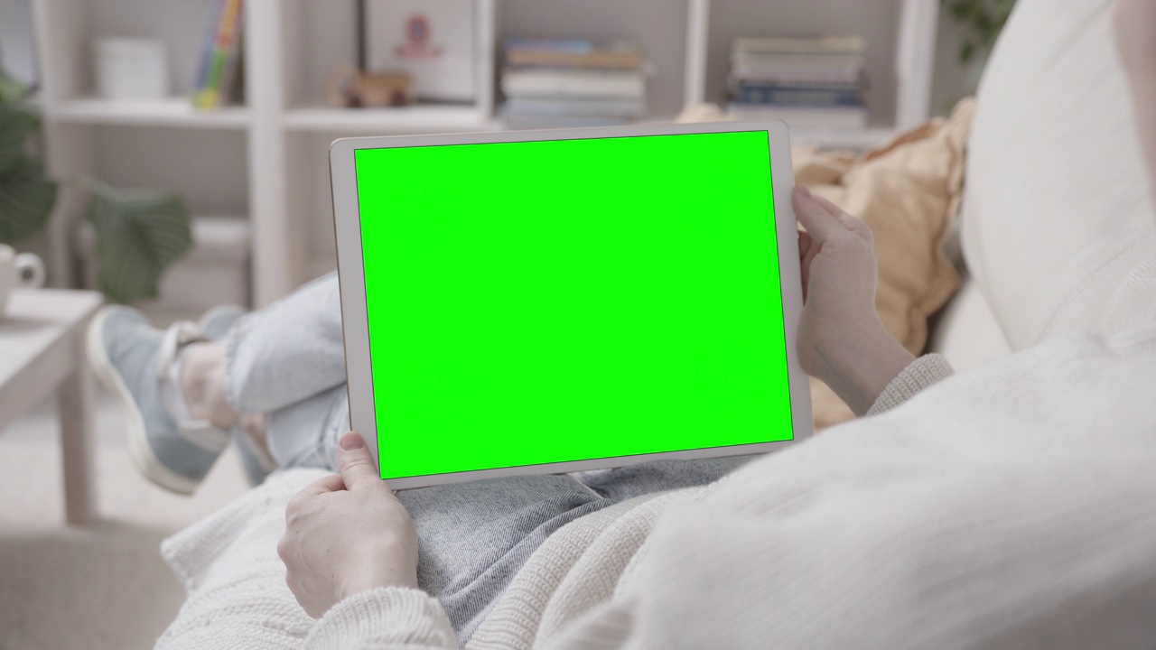 一个女人躺在沙发上，手里拿着平板电脑视频下载