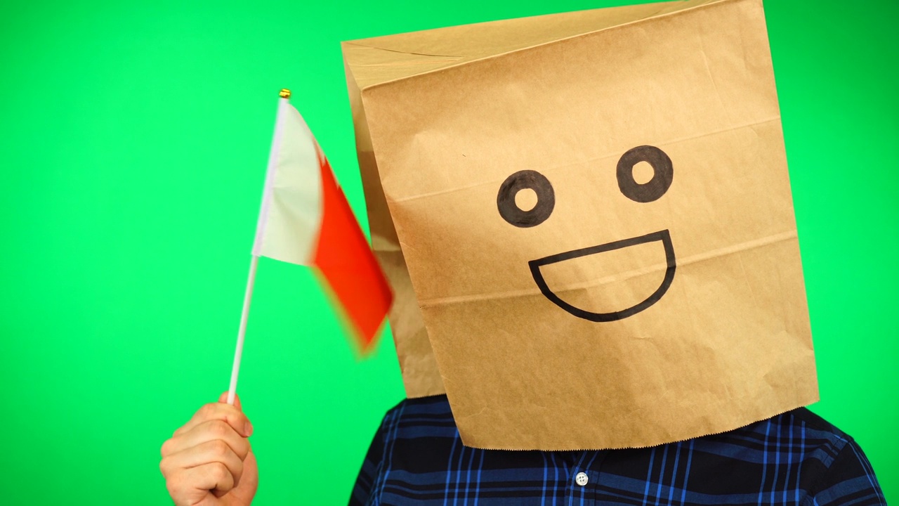 头上戴着纸袋的男子的肖像，在绿色的背景下挥舞着巴林国旗，面带微笑。视频素材