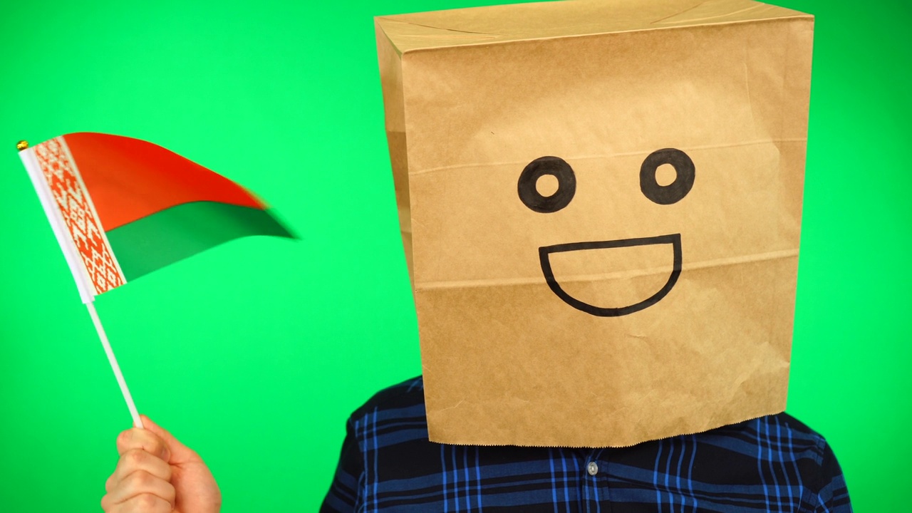 男子的肖像，头上戴着纸袋，在绿色的背景下挥舞着白俄罗斯国旗，面带微笑。视频素材