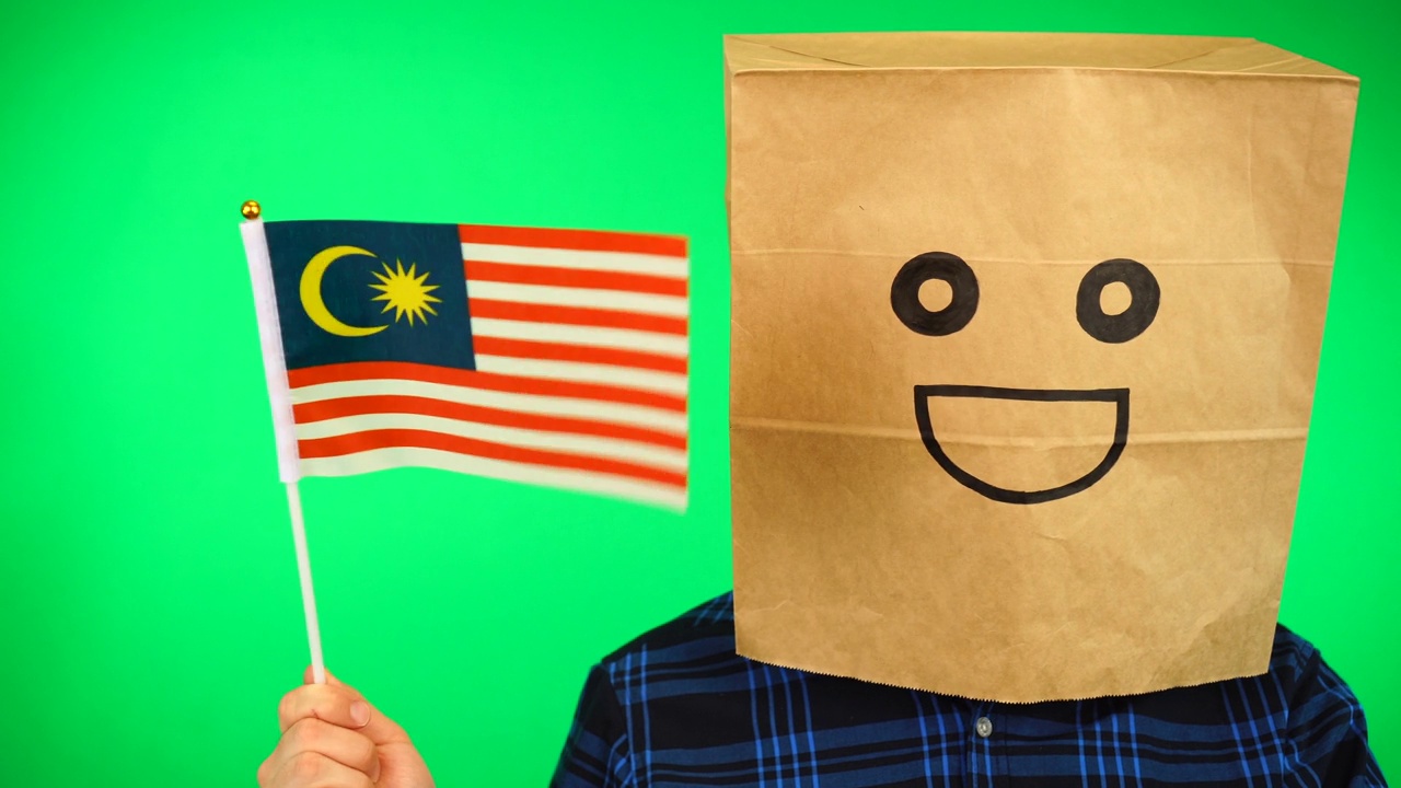 男子的肖像与纸袋在头上挥舞马来西亚国旗与微笑的脸在绿色的背景。视频素材