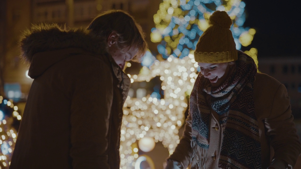 在圣诞树和彩灯的背景下，这对情侣在城市广场上拥抱亲吻视频素材