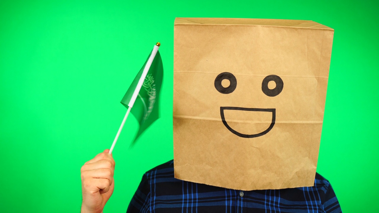 男子头像，头上戴着纸袋，在绿色背景下挥舞着沙特国旗，面带微笑。视频素材