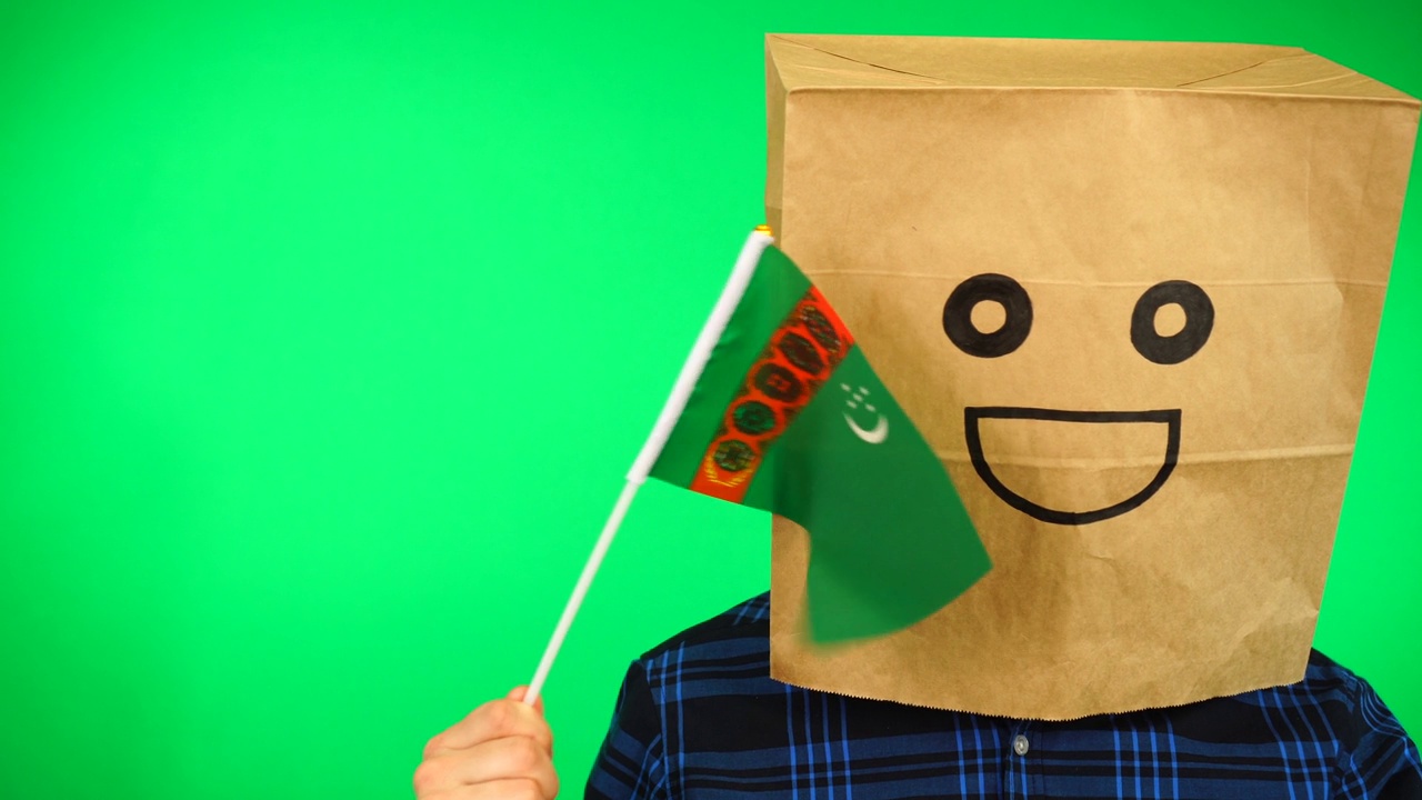 男子的肖像，头上有纸袋，在绿色的背景下挥舞着土库曼斯坦国旗和微笑的脸。视频素材