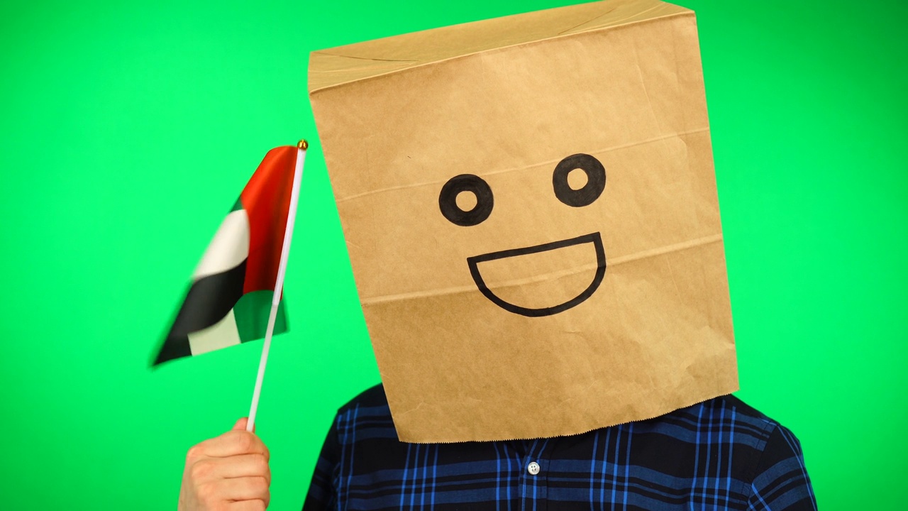 男子的肖像与纸袋在头上挥舞阿联酋国旗与微笑的脸在绿色背景下。视频素材