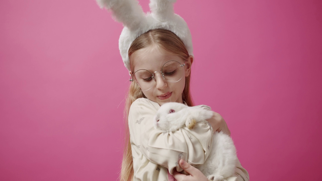 小女孩戴着兔耳朵，手里拿着一只兔子，摆姿势微笑。横幅文本视频下载
