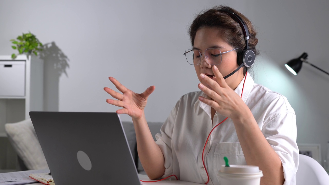 在工作中感到快乐和积极。年轻的亚洲女商人戴着耳机在笔记本电脑上与客户进行视频通话。年轻的亚洲女性提供在线教育课程讲座，咨询客户。视频下载