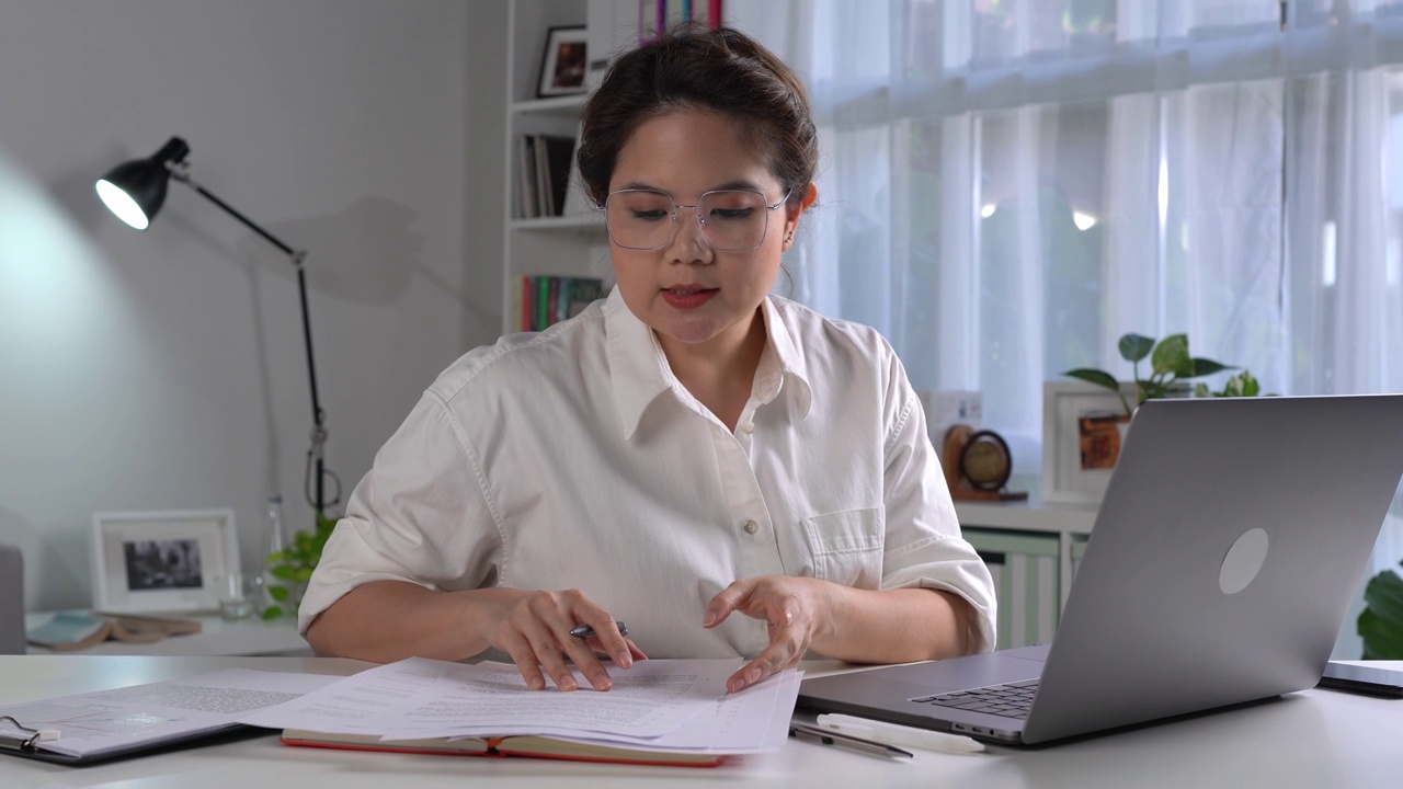 年轻的亚洲女性自由职业者在家里用电脑工作。有吸引力的女商人在线学习，使用笔记本电脑软件，网上冲浪信息或在网上商店购物视频下载