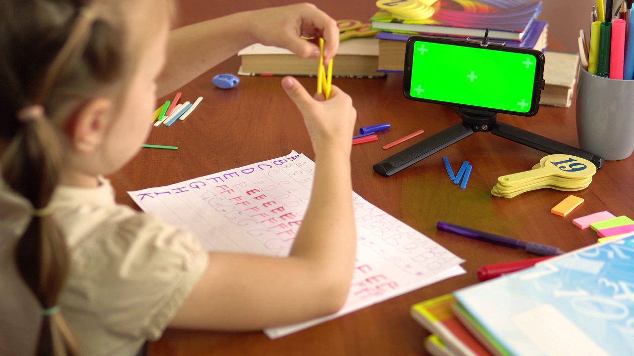 一个学龄前的小女孩展示了计数棒，看着一个绿色屏幕的智能手机。后视图。视频下载
