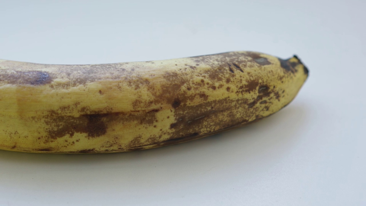 大镜头的成熟香蕉与棕色斑点孤立在白色背景。视频素材
