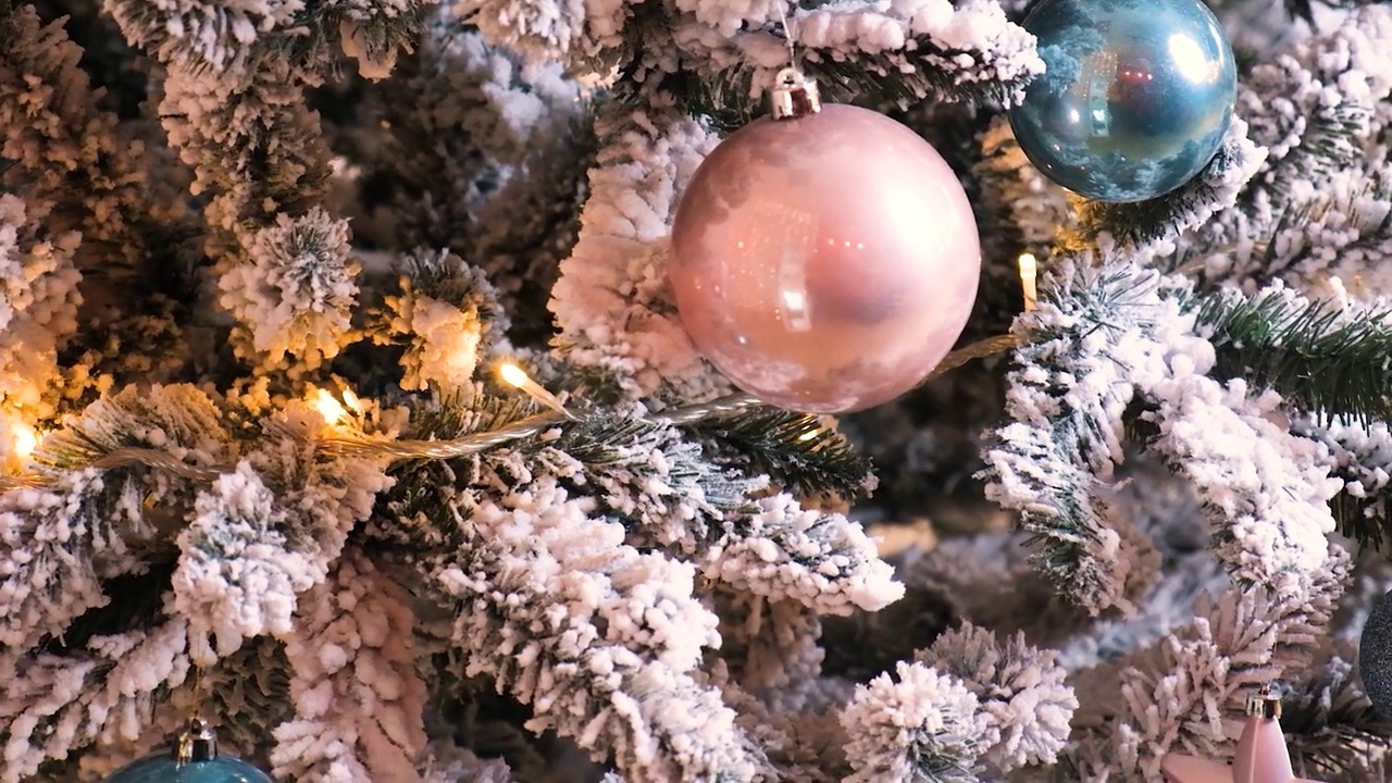 美丽的白雪覆盖的圣诞树，粉红色和蓝色的球，闪闪发光的花环，特写镜头视频下载