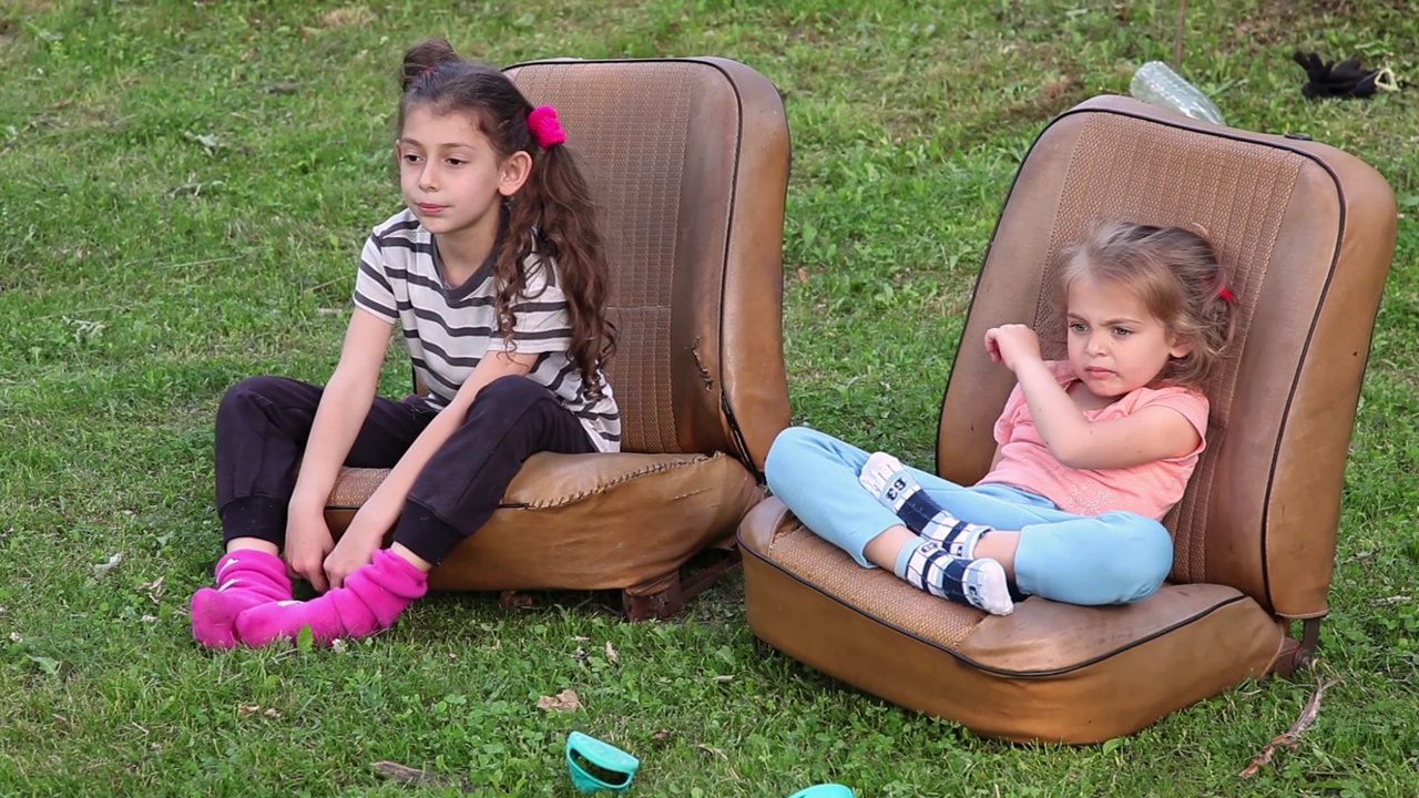 两个小女孩坐在草坪上的汽车座位上视频下载