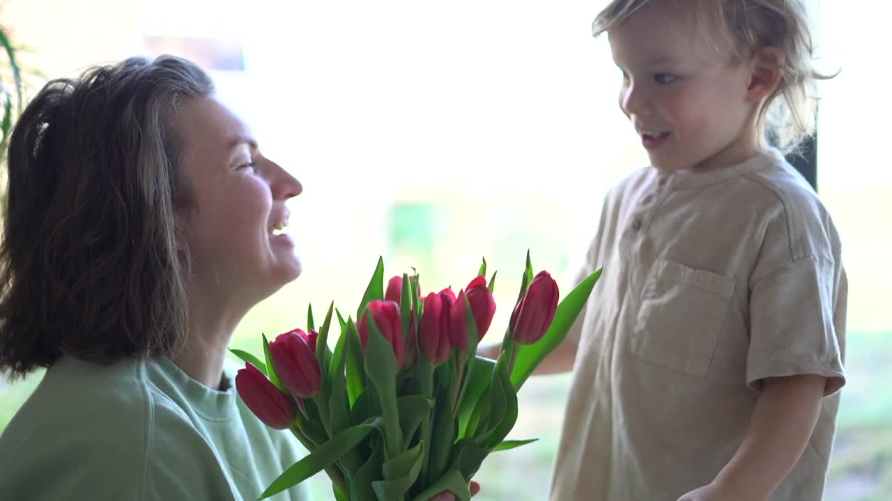 男孩送给妈妈一束粉红色的郁金香，祝贺母亲节。三岁的儿子拥抱和亲吻他的母亲视频下载
