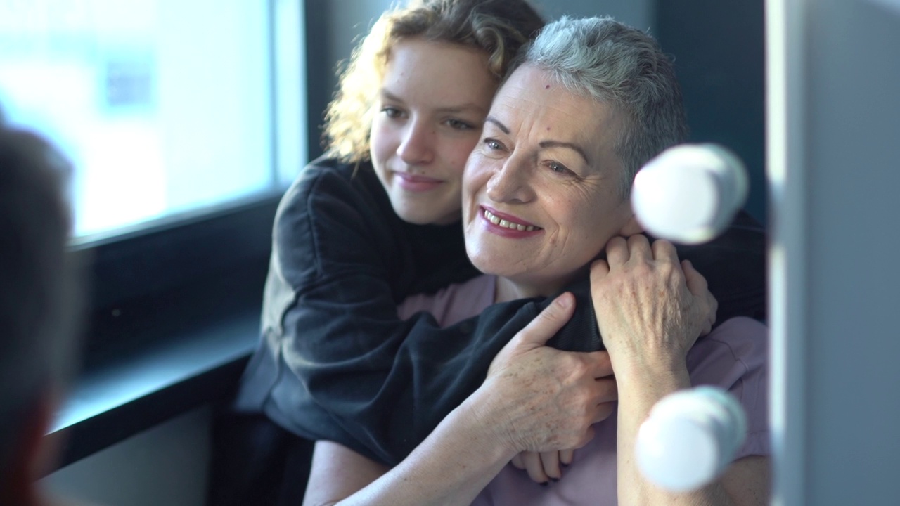 一个十几岁的女孩抱着她美丽的白发苍苍的祖母坐在镜子旁。一个家庭的两代人，与年龄相关的变化和老龄化观念视频下载