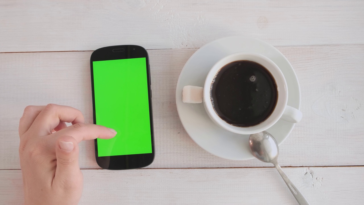 女孩一边喝咖啡，一边用绿色屏幕的手机视频购买