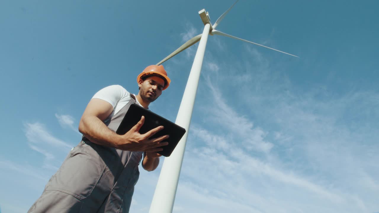 多种族同事使用现代平板电脑检查风力涡轮机。工程师和检查员一起在风车农场工作。两个伙伴一边站在农场上，一边用风车讨论绿色能源视频素材