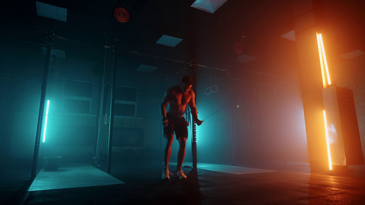 赤裸上身的肌肉男正在用跳绳跳跃。跳绳的男子拳击手。在彩色灯光和烟雾的慢动作中，选手在做跳绳练习。视频下载
