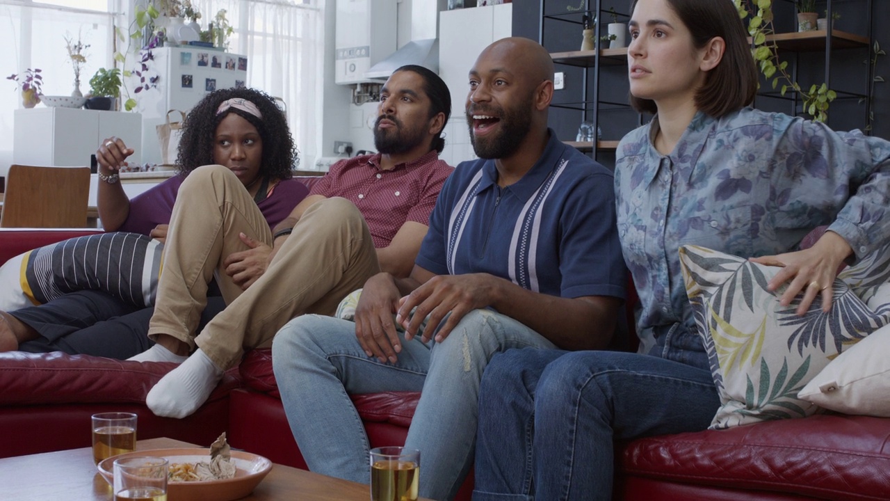 四个多种族的室友在电视上观看比赛并欢呼视频下载