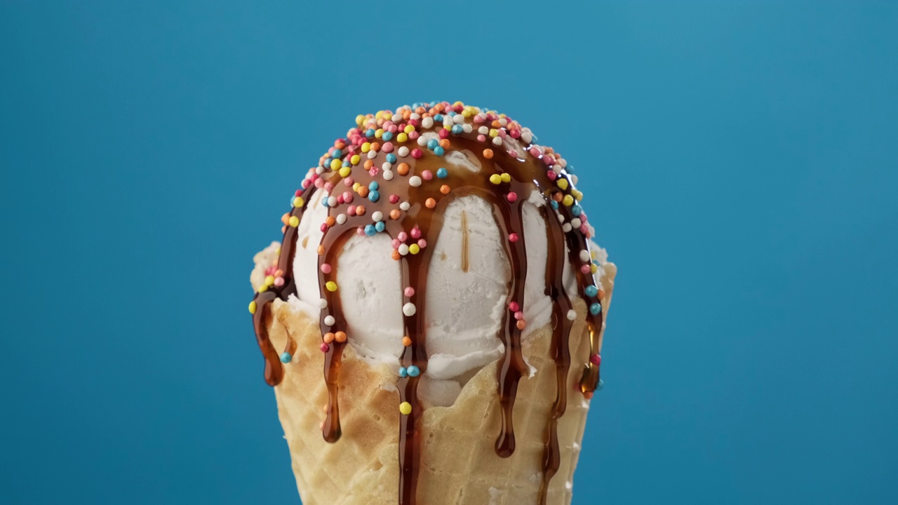 旋转香草冰淇淋在甜筒与焦糖酱在蓝色背景视频素材
