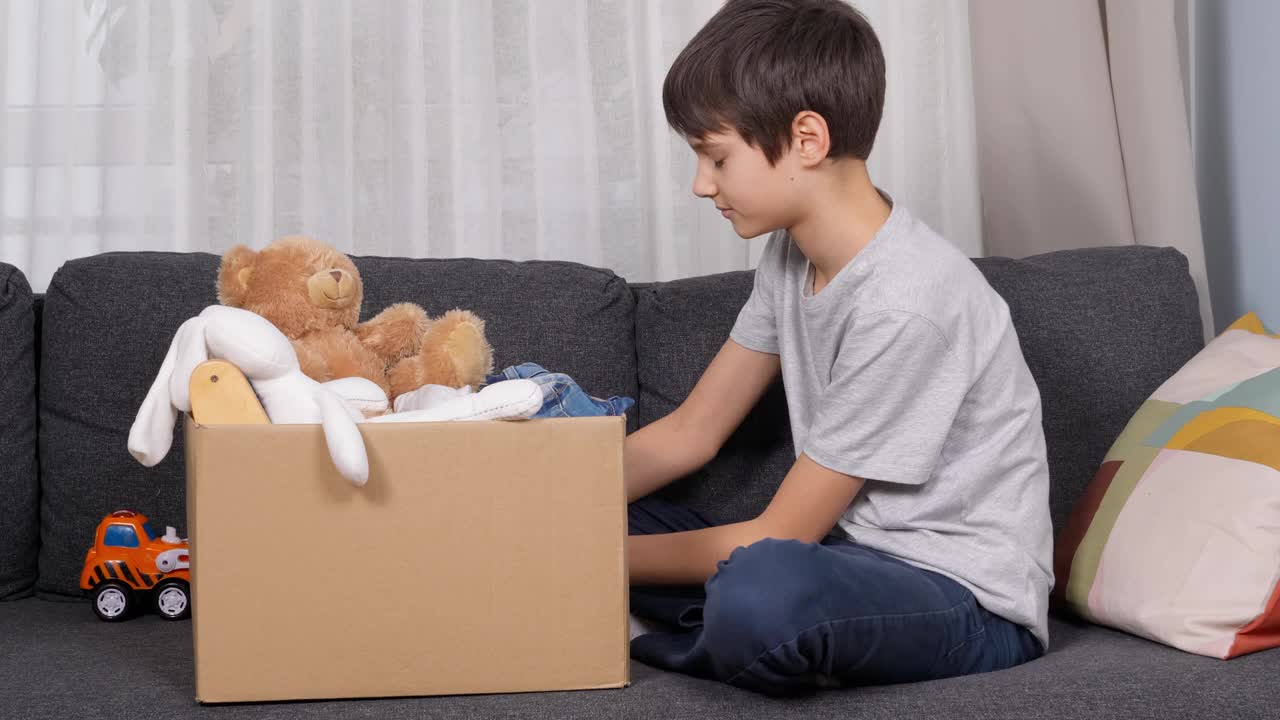 男孩为慈善捐赠准备衣服和玩具。儿童整理和包装儿童玩具，儿童衣服纸箱在家里视频素材