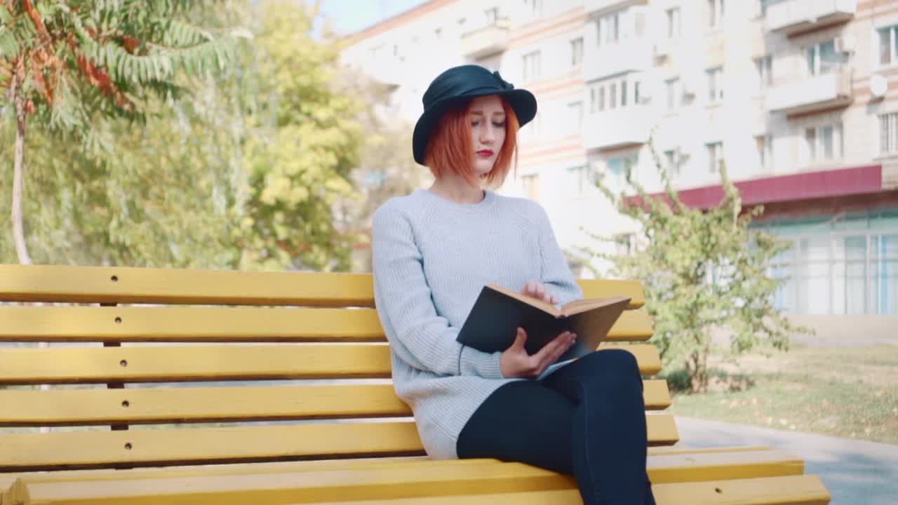 一个女孩手里拿着一本书坐在公园的长椅上。视频素材