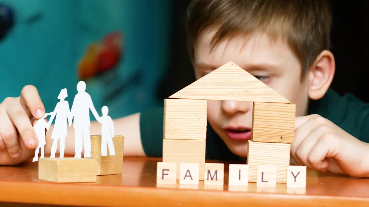 一个孩子在一个家庭中玩耍，一个白人学龄前儿童用立方体建造了一座房子。碑文是一组立方体。一个孩子手里的家庭剪影。孩子的梦想视频下载