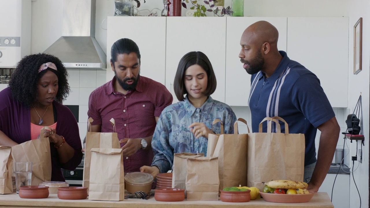 四个来自不同民族的室友从厨房柜台上的袋子里拿出外卖食品视频下载