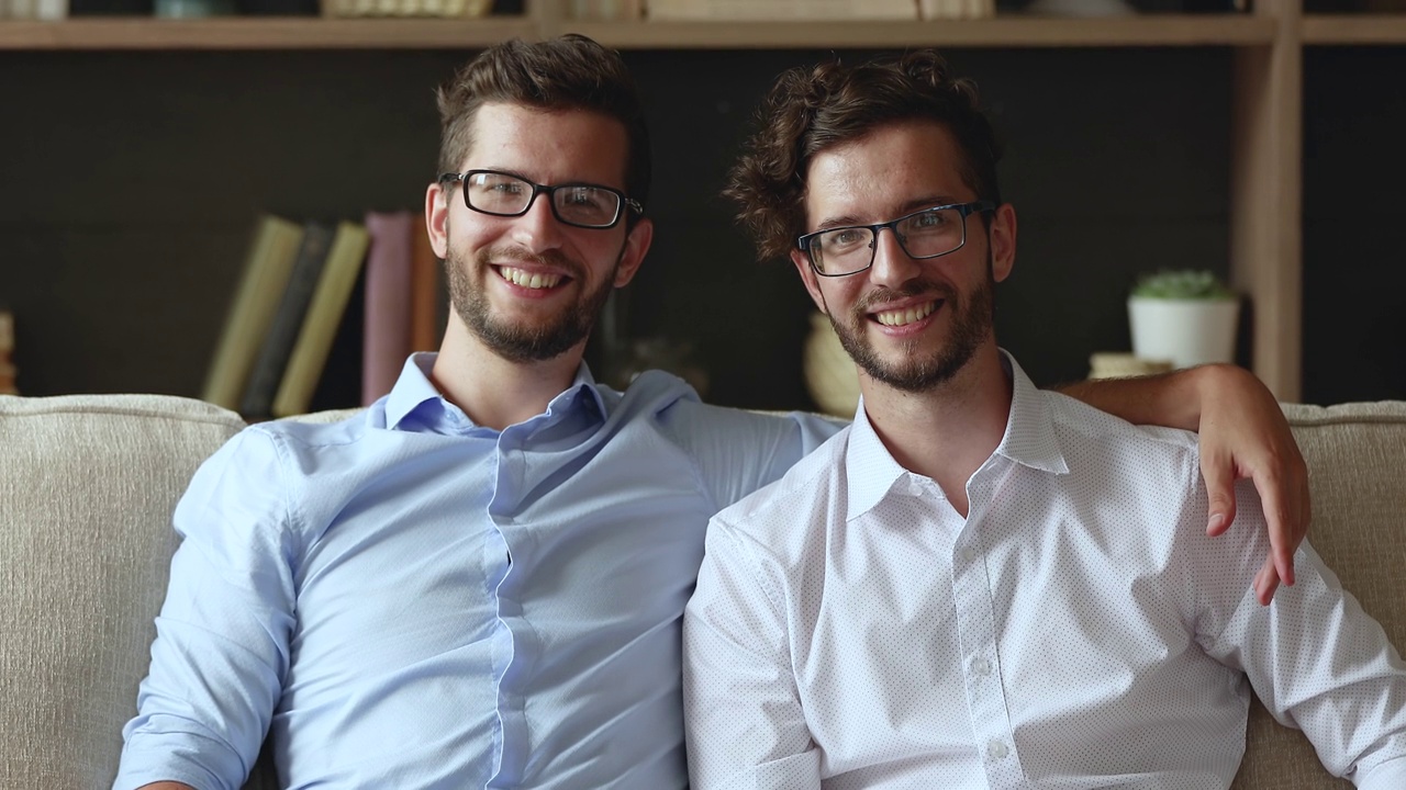 两个快乐的年轻人友好的双胞胎兄弟在沙发上拥抱视频下载