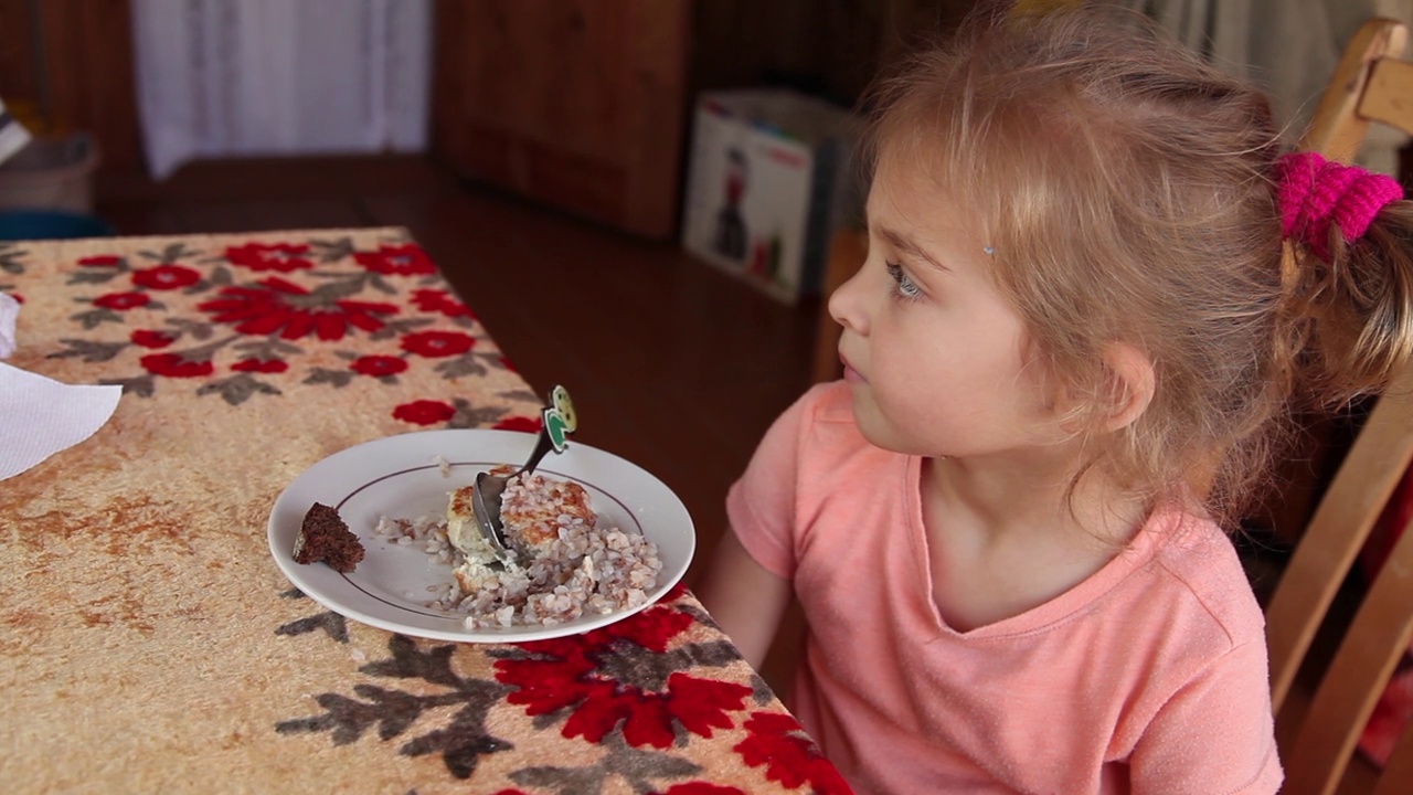 一个小女孩坐在一盘食物前的侧视图视频下载