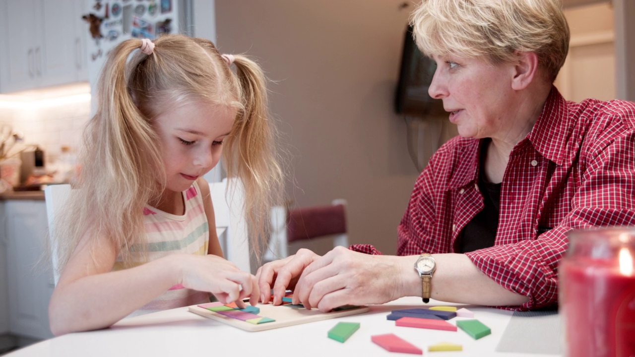 一个成熟的女人，一个年轻的奶奶，正在客厅里和她的小孙女玩拼图。两者都是专注和专注的。视频下载
