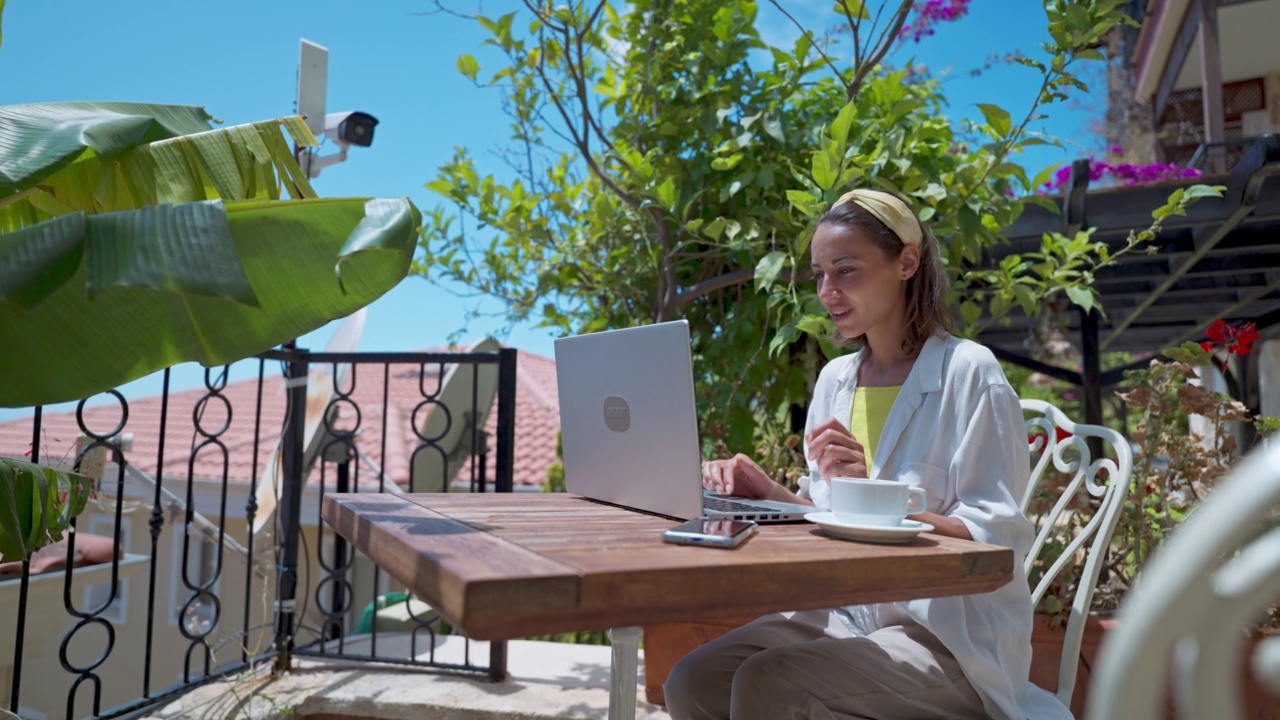 云台镜头dolly特写美丽的女人喝咖啡享受使用笔记本电脑在阳光明媚的日子在度假热带咖啡馆上网视频素材