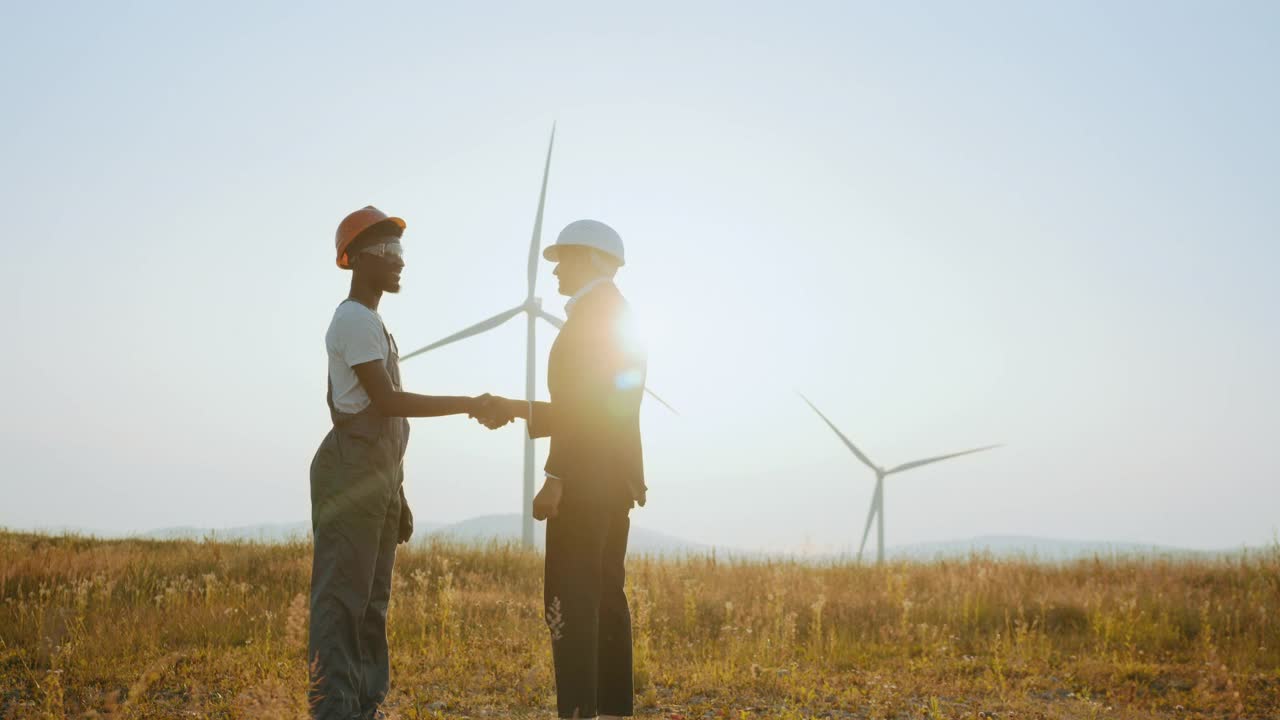 两个同事正在谈成功合作的事。以人为本、团队合作、环保能源。技术人员和非裔美国人检查员在风力涡轮机农场握手视频下载