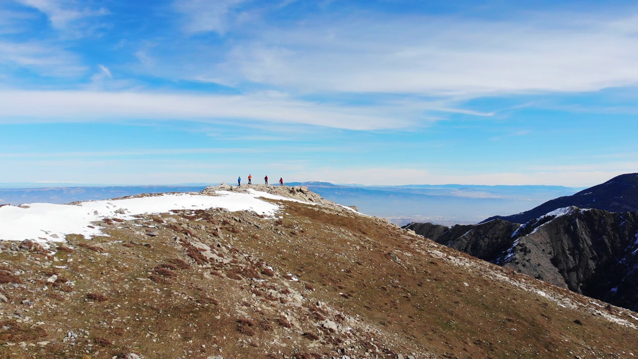 图为，在岩石山的山顶上，登山队员们手持登山杖，观看风景的无人机照片。视频素材
