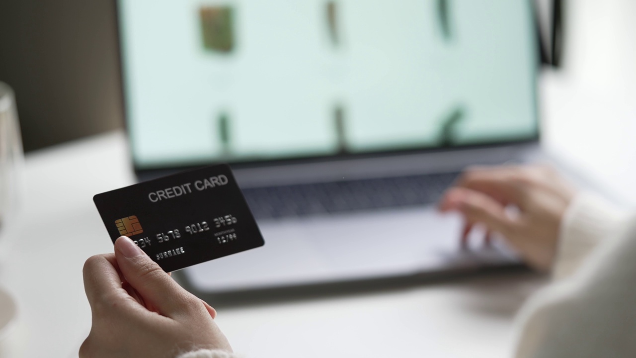 女性手握信用卡，使用笔记本电脑。网上购物视频素材