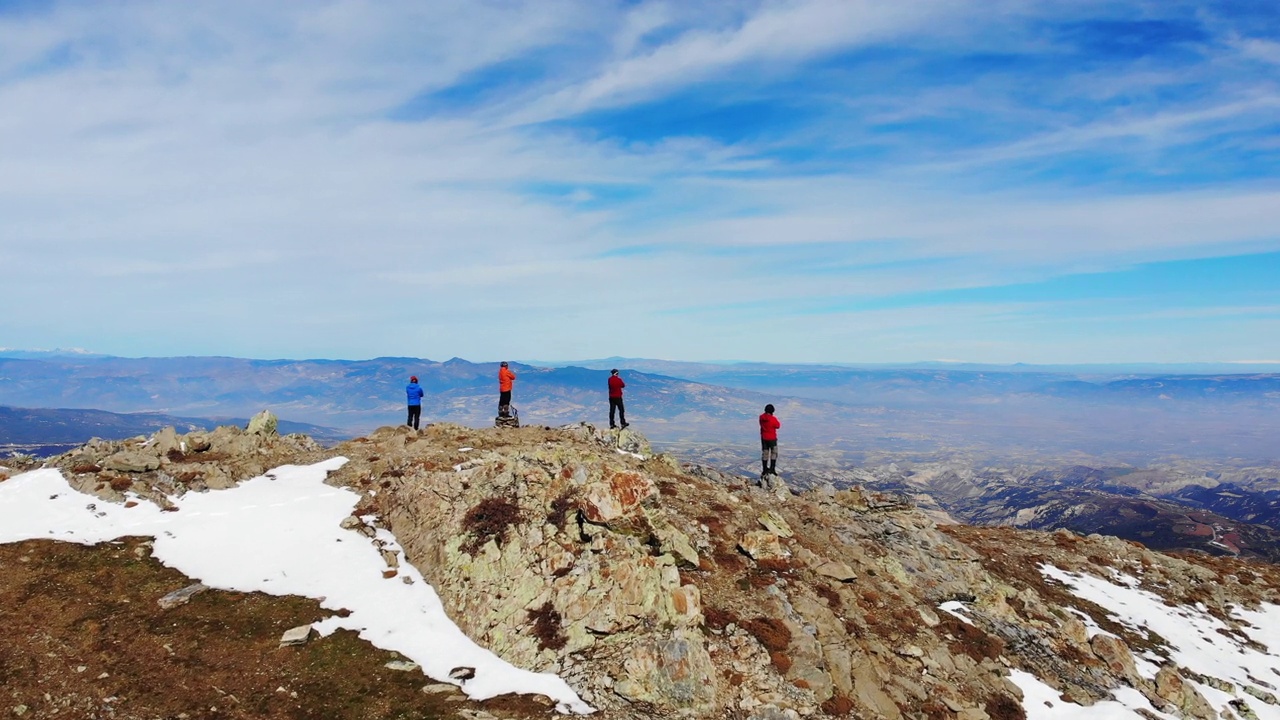 无人机拍摄的是登山队伍交叉双臂站在岩石山顶上观看风景的场景。视频素材