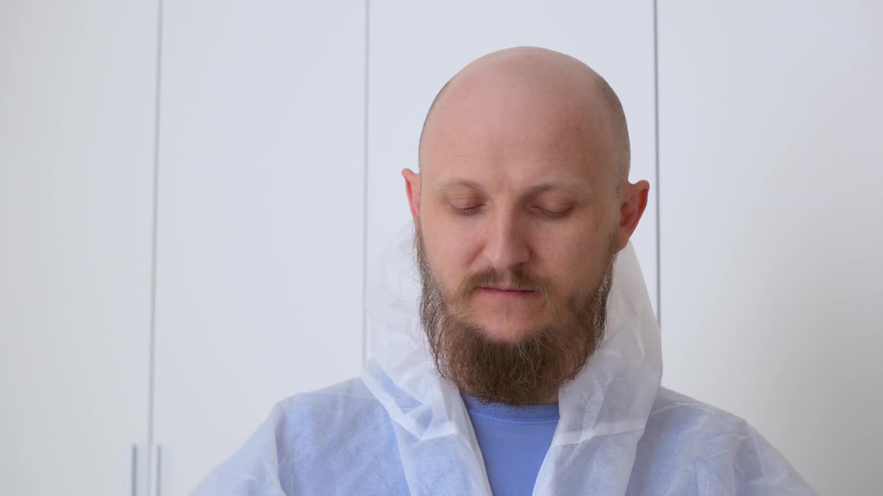 穿着防护服的秃头男子戴上口罩，前往新冠病毒感染地。在新冠病毒感染爆发期间，一名护士在新冠病毒医院的工作视频素材