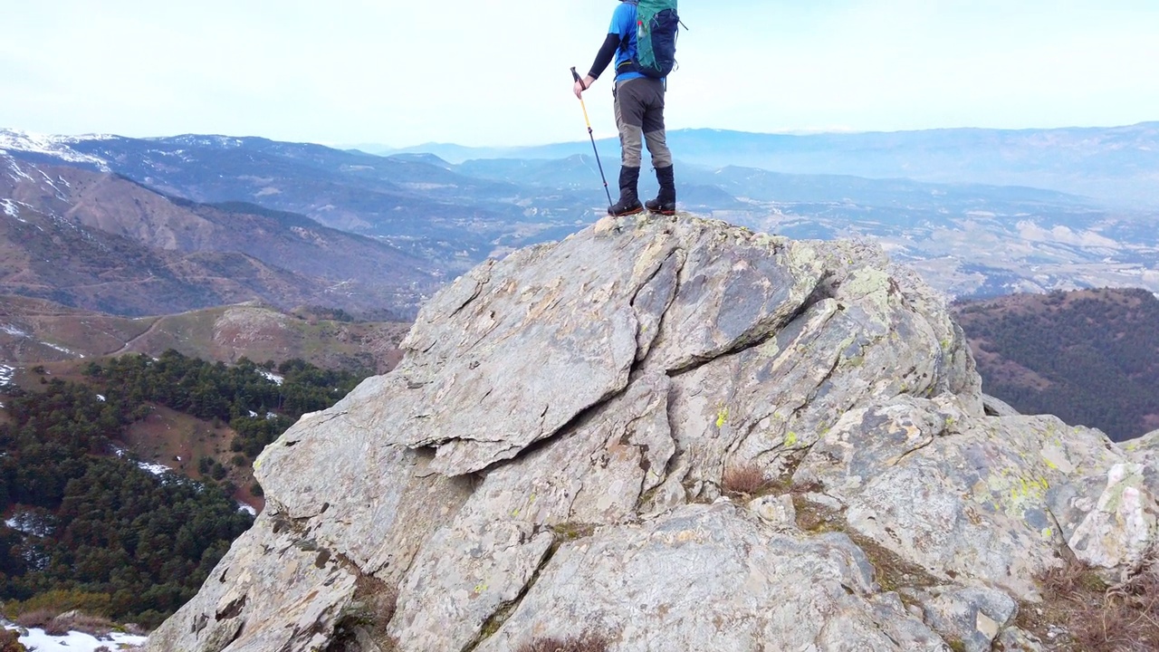 背景摄影师登山运动员是看风景，而持有登山杆在一个岩石山的顶峰。视频下载