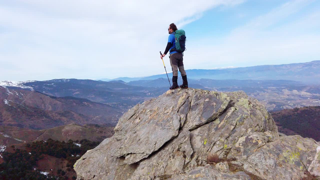 背景摄影师登山运动员是看风景，而持有登山杆在一个岩石山的顶峰。视频素材