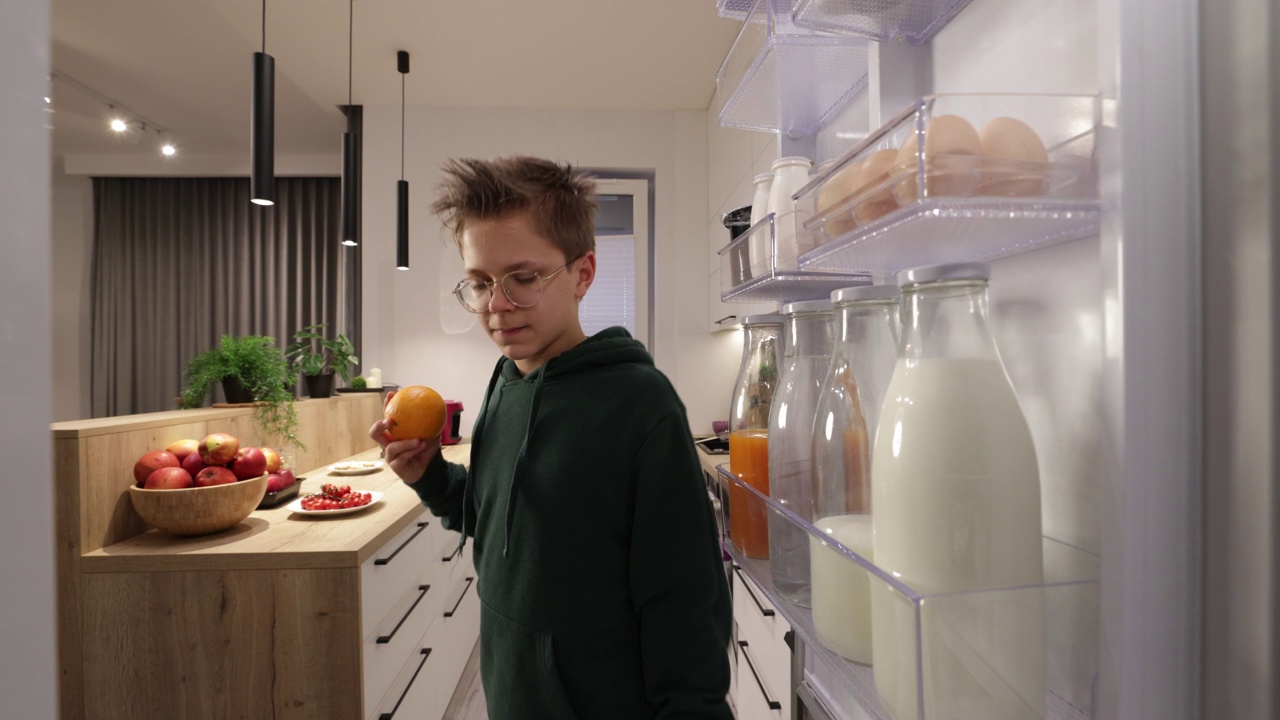 十几岁的男孩从冰箱里拿橘子。视频下载