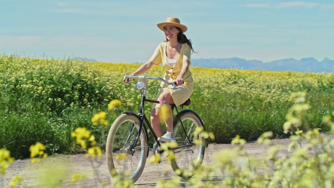 一段4k视频记录了一名年轻女子骑着自行车在乡间的土路上行驶，旁边是一片鲜花视频素材