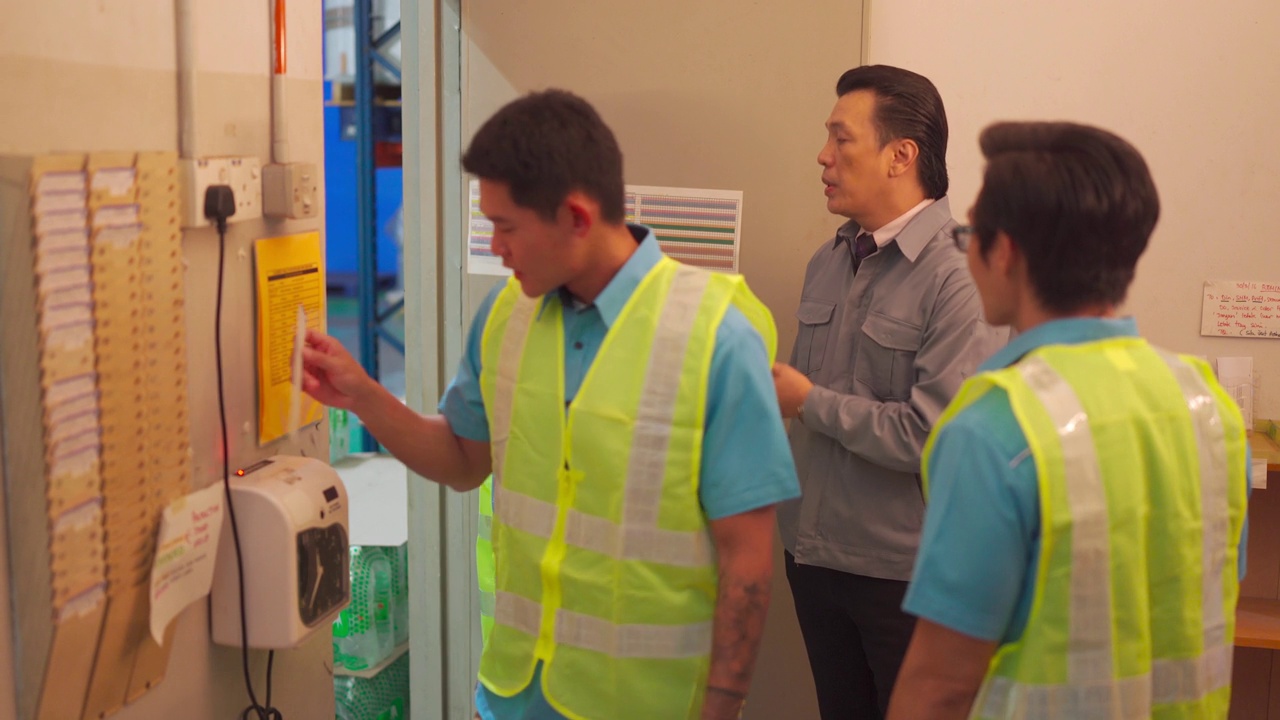 在工厂里，亚洲蓝领工人在时钟卡机旁与他们的主管交谈视频素材