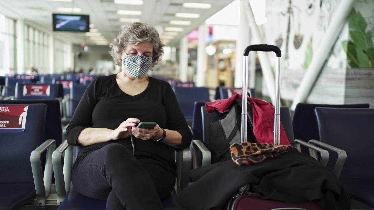 一名戴着面具的成熟女性在机场候机室查看手机视频素材