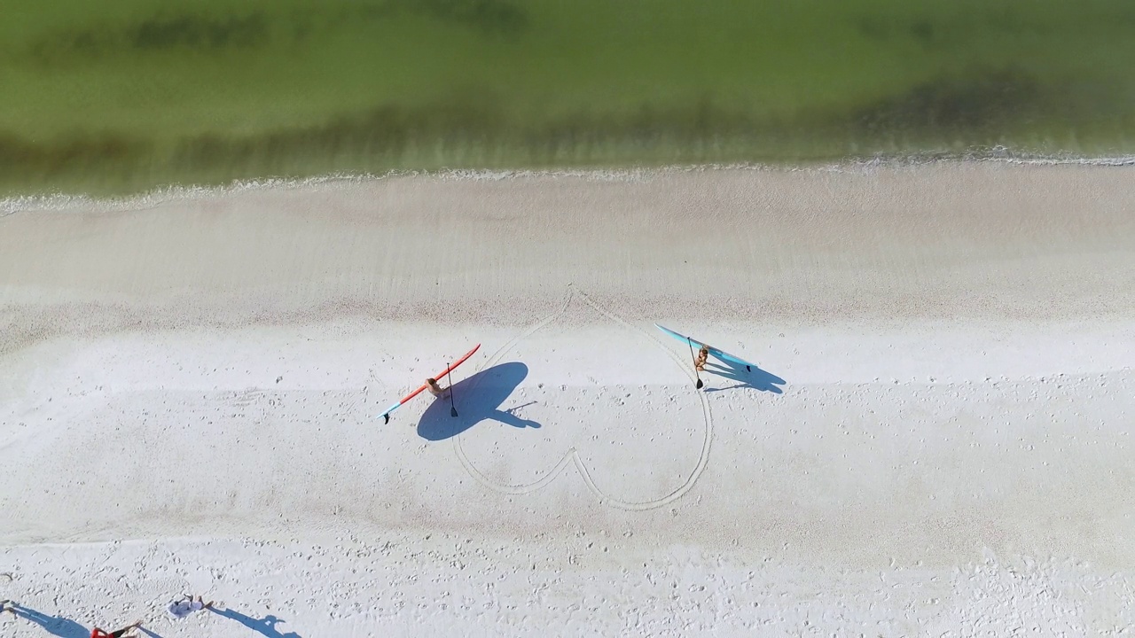 男人和女人用桨板在沙滩上形成心形视频下载