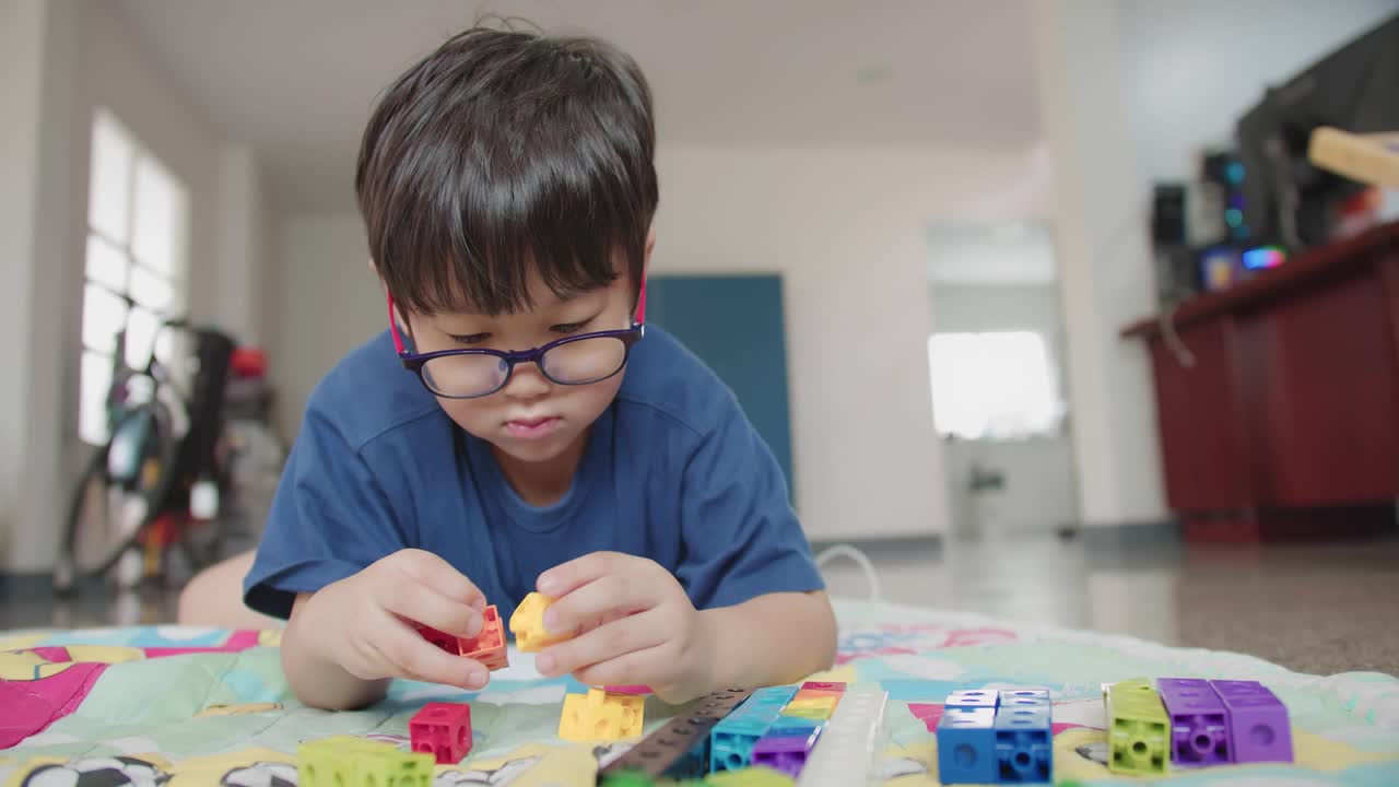 肖像吸引人的聪明可爱的亚洲孩子男孩戴着眼镜享受在客厅玩五颜六色的高楼大厦视频下载