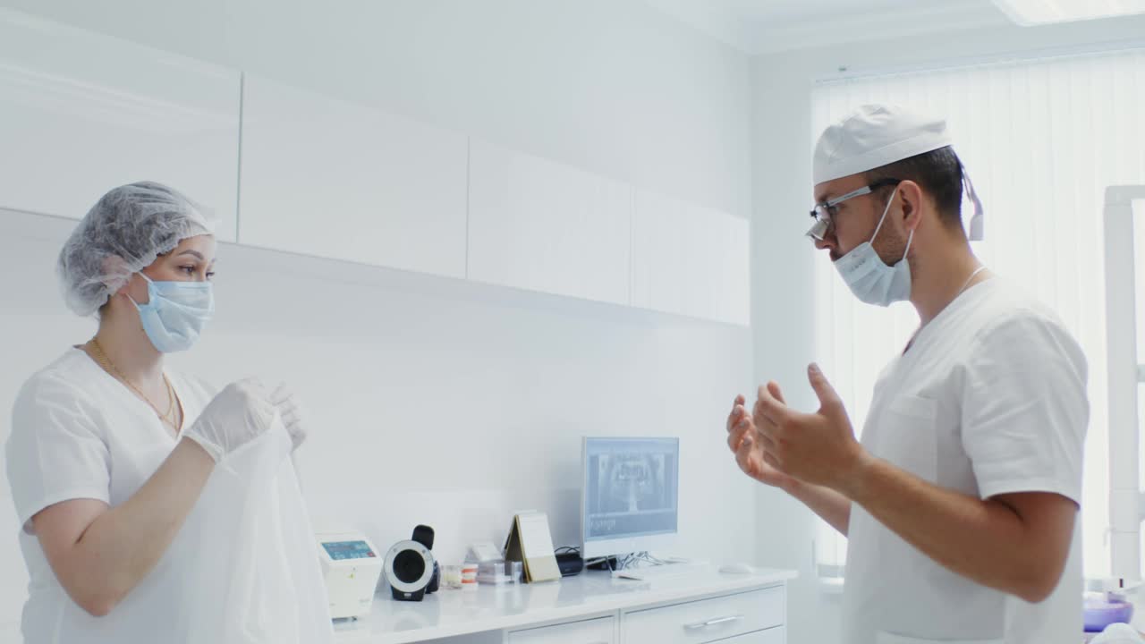 护士帮一个牙医穿上白色的无菌服，系好他背上的领带视频素材