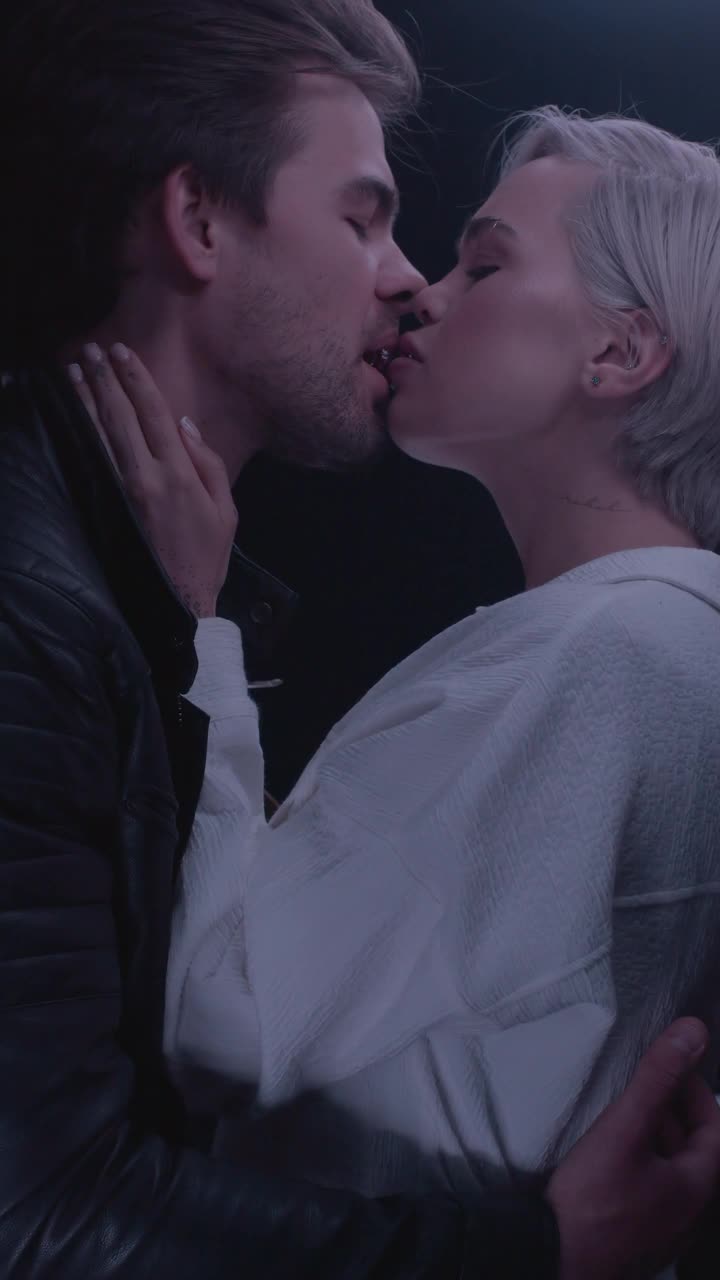年轻感性夫妇的肖像拥抱，亲吻在现代动态光室内近。视频素材